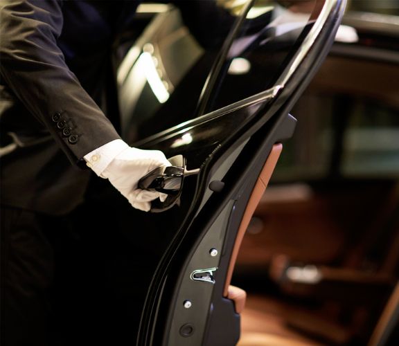 A chauffeur in a suit and white gloves opening the door of a luxurious black limousine.