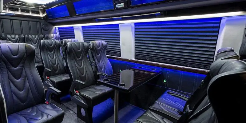 Executive Mercedes Sprinter interior setup with leather recliner seats, conference table, and privacy window shades