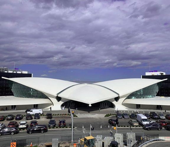 TWA Flight Center terminal at John F. Kennedy International Airport under a cloudy sky, cars parked in front