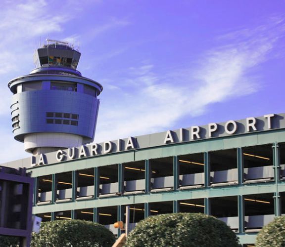LaGuardia Airport sign on the terminal building with the control tower behind it